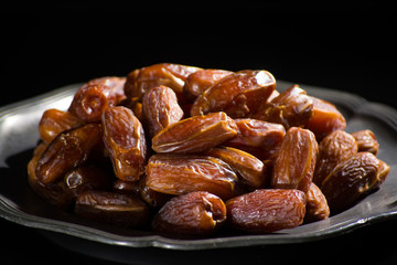 Sweet dessert dried date in old tin bowl, low key, dark theme, on black background with reflection