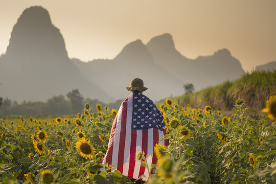 A man is walking into the sunflower field with United State flag as in independence day and freedom concept with landscape mountain background while sunset.