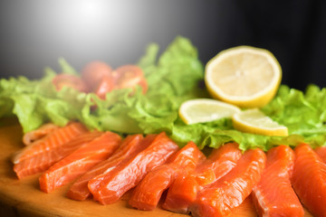 pieces of red fish with lemon and cherry tomatoes on a wooden board on a black background
