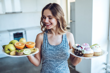 Young woman choosing between fruits and sweets
