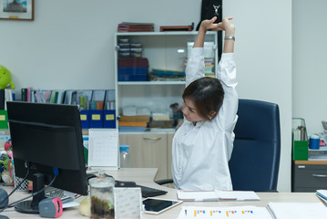 Asian officer woman stretching body at the desk of office from back angle,Thailand people,Businesswoman tired from hard work