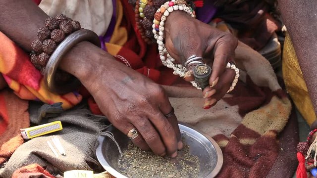 Hindu sadhu man preparing a cigarette to smoke marijuana with chillum on the ghats of the Ganges river in Varanasi, India . Close up
