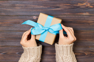 Woman hands give wrapped valentine or other holiday handmade present in paper with blue ribbon....
