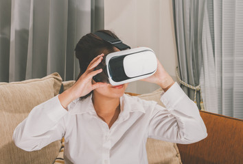 Asian woman wearing virtual reality glasses expressing  on brown sofa, smartphone using with VR glasses