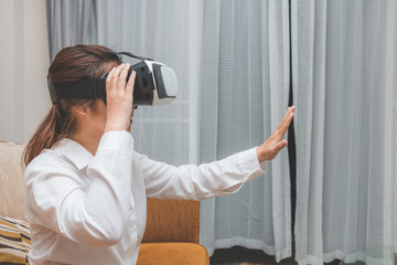 Asia woman wearing virtual reality goggles and enjoy to try touching on brown sofa, Innovation technology