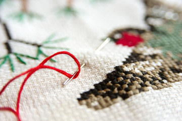 Cross-stitch embroidery and needle with red thread. Red bullfinch on a fir-tree embroidery macro close up. View from above.