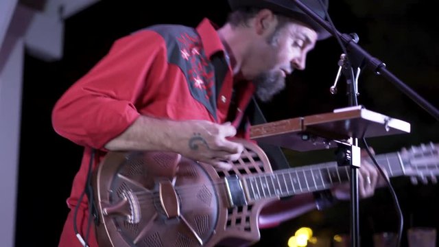 Closeup of guitarist playing a resonator at a live performance outside at night.