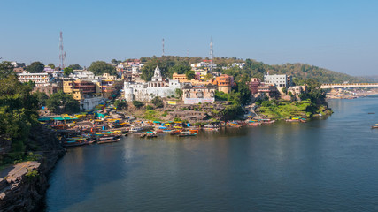 Fototapeta na wymiar Omkareshwar cityscape, India, sacred hindu temple. Holy Narmada River, boats floating. Travel destination for tourists and pilgrims.