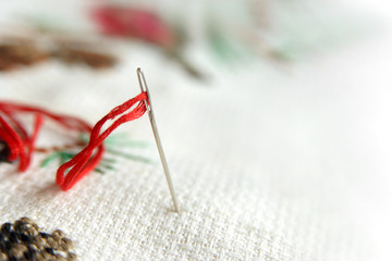 Cross-stitch embroidery and needle with red thread. Embroidery macro close up. View from above. Free copy space.