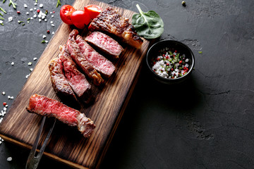 Rib eye steaks and spices on wood at black background