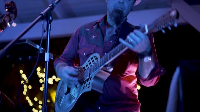 Closeup of roots music resonator guitar player rocking to the music at an outdoor concert at a restaurant.