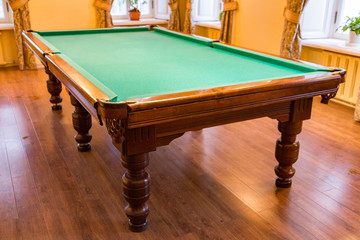 Large wooden table with green cloth for playing billiards
