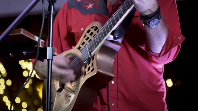 Closeup of resonator guitar as musician performs live at an outdoor venue at night.s