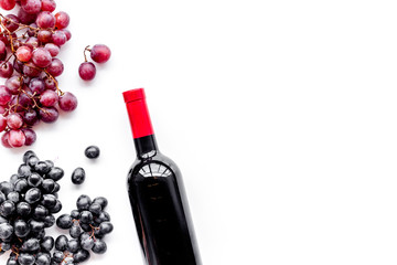 Bottle of red wine near bunch of grapes on white background top view copyspace