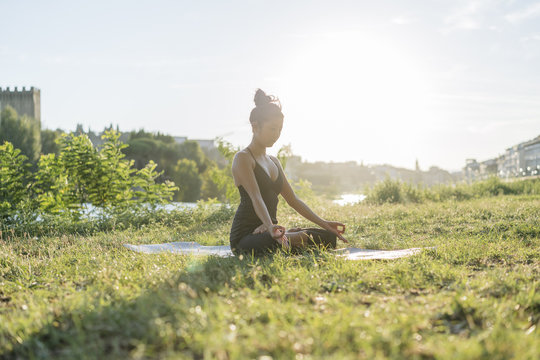 Young Japanese woman practicing yoga exercises near a river in a summer day in the city