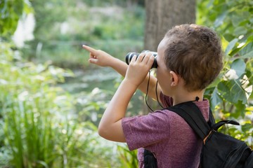 Boy looking through binoculars and pointing in the forest