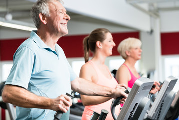 Happy seniors train on cross trainer with personal trainer at the gym