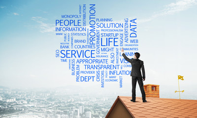 Young businessman standing on house roof and writing leadership skill concept. Mixed media