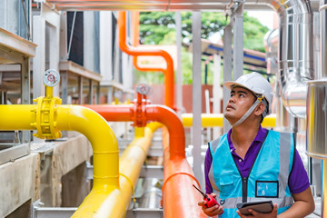 Asian engineer wearing glasses working in the boiler room,maintenance checking technical data of heating system equipment,Thailand people