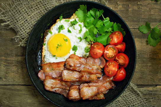 Fried egg with bacon, tomatoes and parsley in frying pan, top view