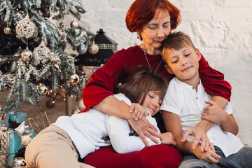 Pretty old lady in red dress poses with her grandchildren before a Christmas tree