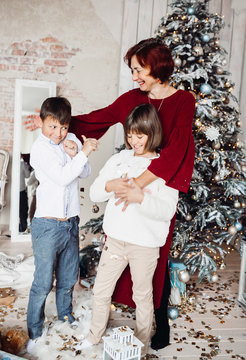 Pretty old lady in red dress poses with her grandchildren before a Christmas tree