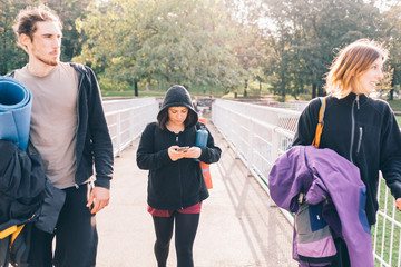 Three young beautiful caucasian sportive friends walking outdoor in the city backlight chatting -...