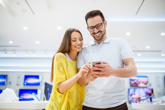 Close up of focused smiling couple in love choosing and holding a mobile in a tech store.