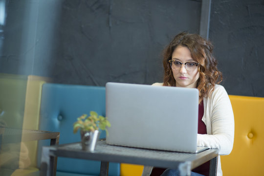studentessa con gli occhiali è immersa davanti al suo computer in un locale con divani coloratie