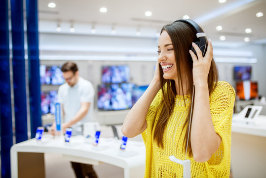 Close up of adorable attractive happy girl testing headphones in a tech store.