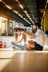 Side view of attractive beautiful sporty muscular shape couple sitting in front of the mirror while man massaging his girlfriend in the sunny gym.