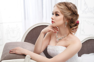 A sweet bride in a beautiful dress sits in an armchair in a chic, light interior.