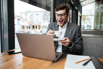 Laughing business man in eyeglasses sitting by table in cafe