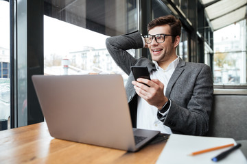 Cheerful business man in eyeglasses sitting by table in cafe