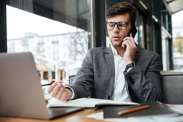 Confused business man in eyeglasses sitting by table in cafe