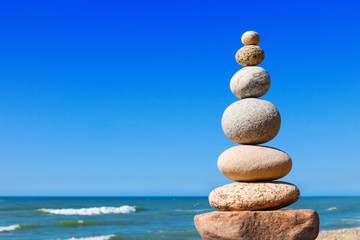 Rock zen pyramid of white and pink stones on a background of blue sky and sea.