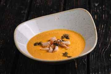Pumpkin cream soup with shrimp on dark wood background