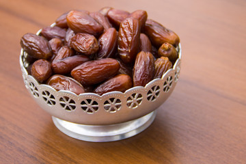 Dates fruit on a silver bowl on wooden table. The Muslim feast of the holy month of Ramadan Kareem