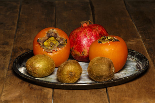 Persimmon, kiwi, pomegranate on a platter on a wooden table.