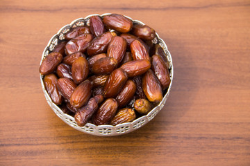 Dates fruit on a silver bowl on wooden table. The Muslim feast of the holy month of Ramadan Kareem