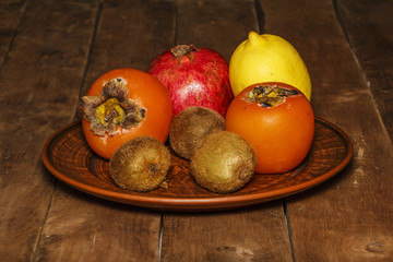 Persimmon, kiwi, pomegranate on a platter on a wooden table.