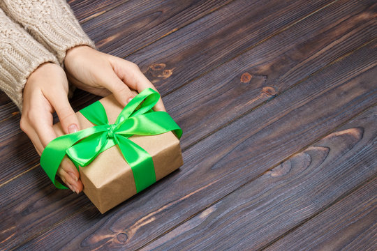 Woman's hands give wrapped valentine holiday handmade present in craft paper with green ribbon. Present box, decoration of gift on black wooden table, POV with copy space