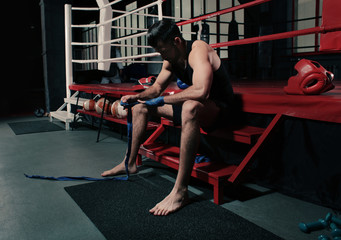 Fototapeta na wymiar Male boxer applying hand wraps while preparing for training in gym
