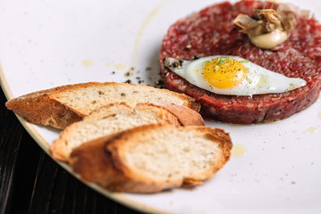 Beef tartare with fried quail egg served with bread on dark wood background
