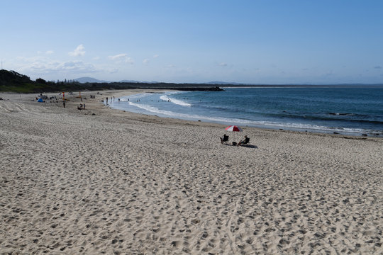 Badestrand mit Sonnenschirm und zwei Personen im rechten Drittel und viel Sand im vorderen Bereich