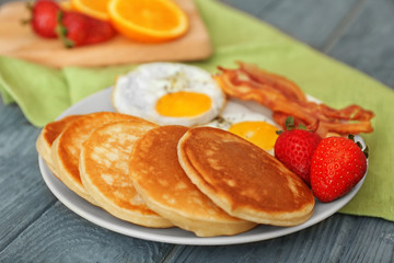 Plate with yummy pancakes, strawberry, fried eggs and bacon on wooden table
