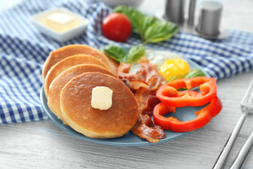 Plate with yummy pancakes, pepper, fried egg and bacon on wooden table