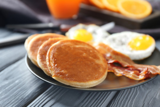 Plate with yummy pancakes, fried bacon and eggs on wooden table