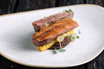 Duck fillet with polenta on irregular shape plate on dark wood background