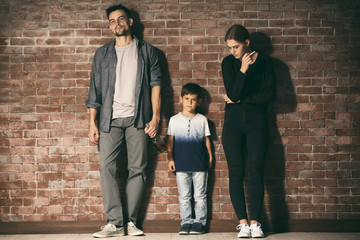 Man and woman standing near their little son with bottle of alcohol and cigarette against brick wall background